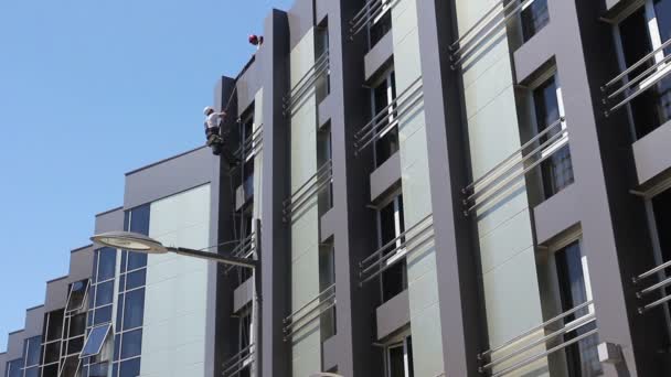 Teamwork at industrial climbers, washing building facade. Industrial climbers are adjust climbing gear together for washing, cleaning facade of a modern office building. - Footage, Video
