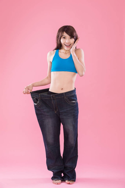 驚いた女性のジーンズを着て、ピンク色の背景で体重減少を示す  - 写真・画像