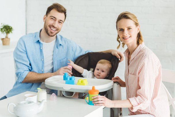 Parents with feeding bottles and infant daughter in baby chair with plastic blocks - Photo, image