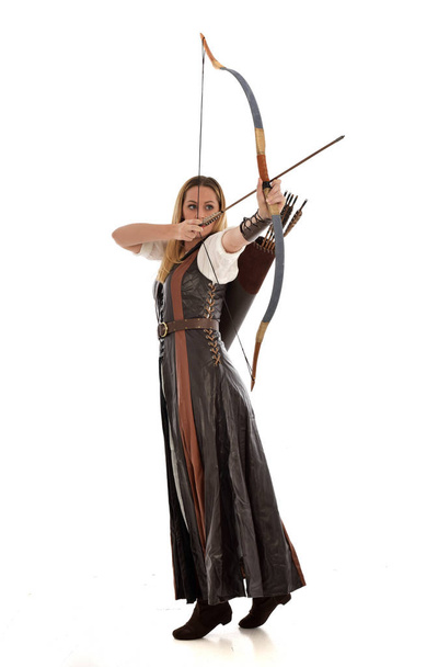 ritratto a figura intera di donna vestita con fantasia medievale marrone, con arco e freccia. in piedi posa su sfondo bianco studio
. - Foto, immagini