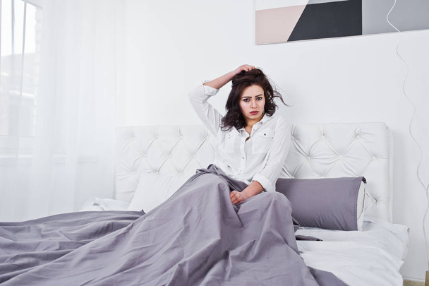 Studio portrait of brunette girl in white blouse lying on bed. - Photo, Image