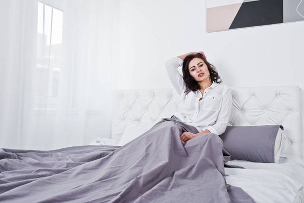 Studio portrait of brunette girl in white blouse lying on bed. - Foto, imagen