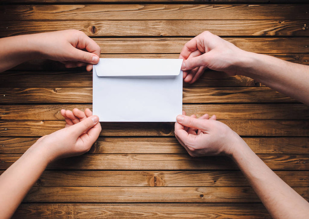 Hands hold a white paper envelope. Clean sheet of paper on a wooden background. - Fotoğraf, Görsel