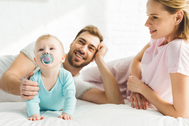 Smiling parents and infant daughter with baby dummy in bed - Fotografie, Obrázek