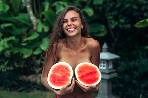 Portrait beautiful brunette girl in swimsuit with watermelon fruit holding in hands. Sexy model with perfect body, cute smile posing. Concept of sport, vegetarian and healthy food - Foto, Bild