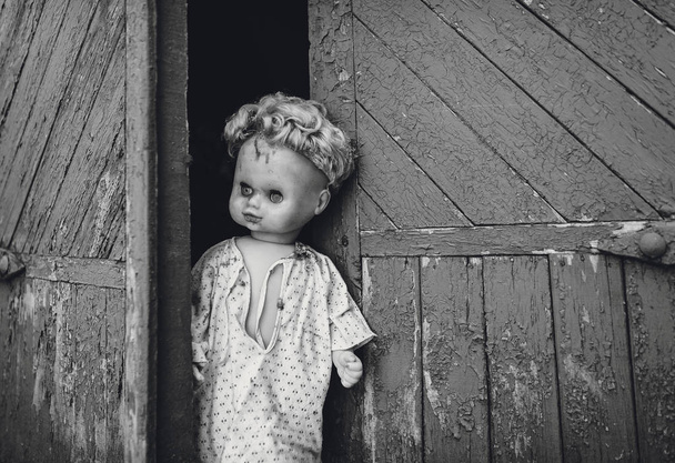The old doll sitting in the doorway. Old wooden shed. Fear, hate, horror, loneliness. Vintage. - Фото, зображення