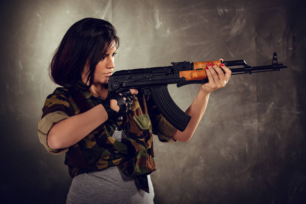 Menina atraente em pé na atitude de mirar e olhar através da mira rifle automático
. - Foto, Imagem