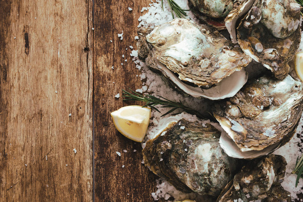 Open shell oester met citroen en zout op een houten plank - Foto, afbeelding