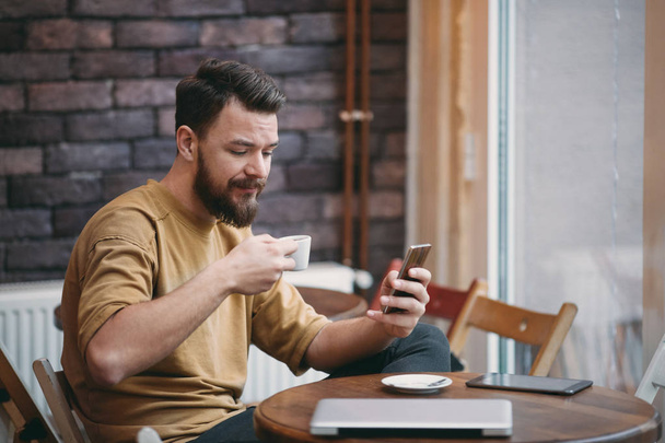 Fiatal ember ül a kávézó, és intelligens telefon használata. - Fotó, kép