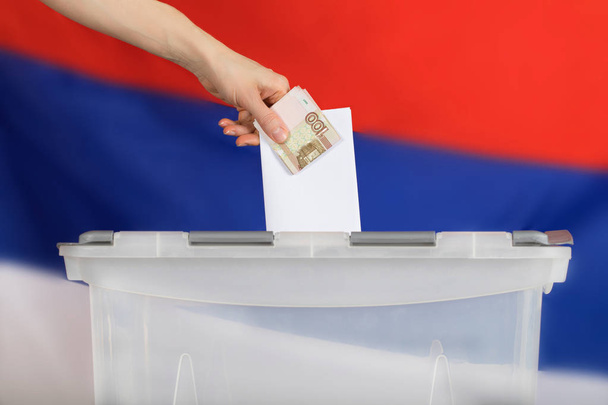 Naisten käsi pitää äänestyslippua ja Venäjän ruplaa äänestyslipukkeen yläpuolella b
 - Valokuva, kuva