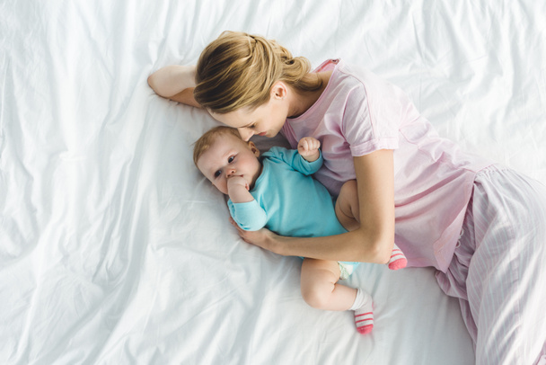 High angle view of smiling mother with infant daughter in bed - Photo, Image