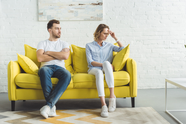Upset couple sitting after argue on couch in front of wall with painting - Foto, imagen