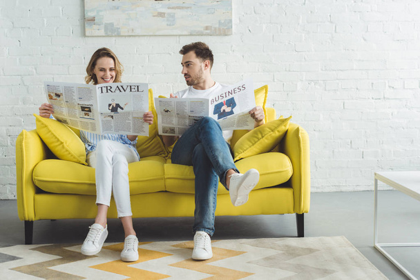 Empresário com esposa lendo jornais sobre viagens e negócios enquanto se senta no sofá na sala moderna com pintura
 - Foto, Imagem
