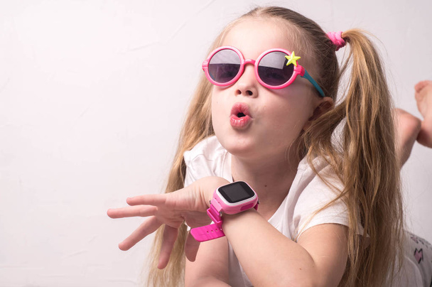Technology for children: a girl wearing pink glasses uses a smartwatch. - Photo, image