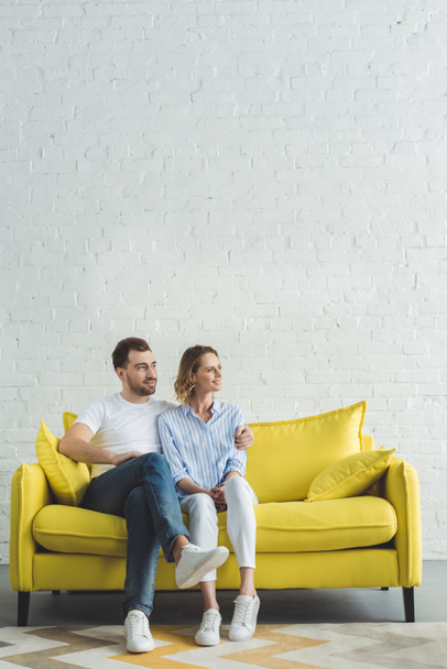 Young man embracing girlfriend on yellow sofa in modern room - Fotografie, Obrázek