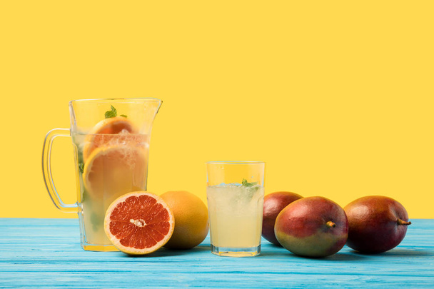 frische Mango mit Grapefruits und kaltem Sommergetränk in Glas und Krug auf türkisfarbener Holzplatte  - Foto, Bild