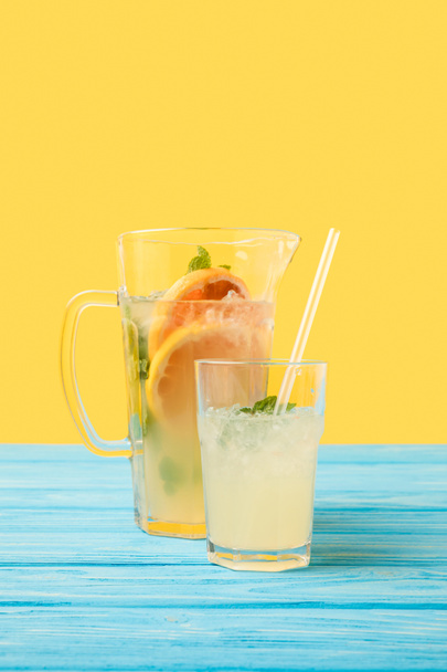 Close-up beeld van verse koude zomer drank in glas en kruik op geel - Foto, afbeelding