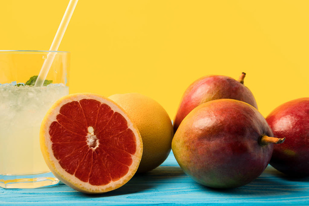 vista de cerca de pomelos y mangos frescos y maduros y vidrio con bebida fría de verano en amarillo
 - Foto, Imagen