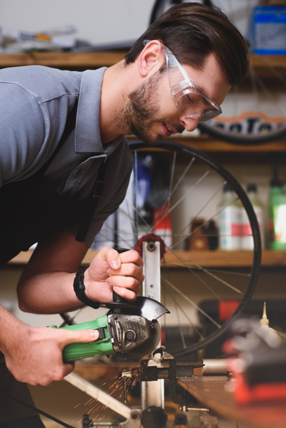 young man in protective goggles holding angle grinder in workshop - Photo, Image