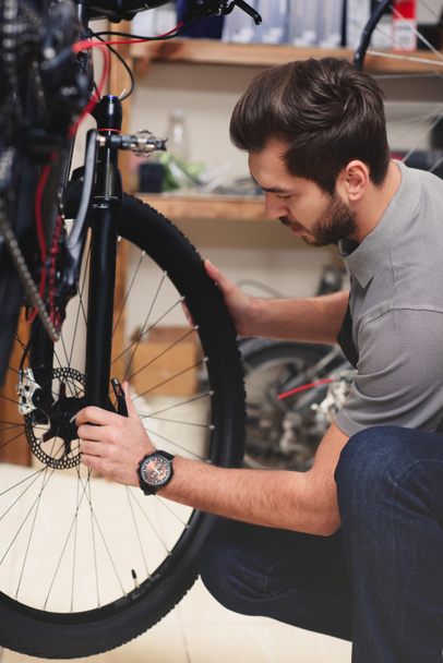 young male worker in apron fixing bicycle in workshop - Foto, Bild