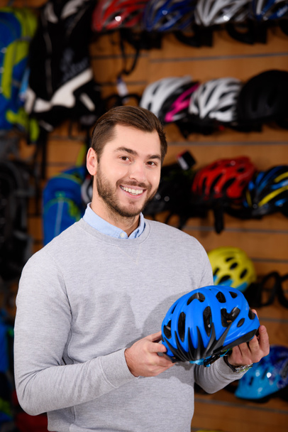 handsome young man holding bicycle helmet and smiling at camera in workshop - Photo, Image