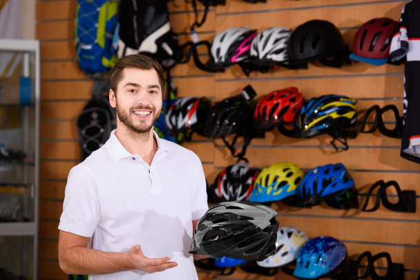 giovane operaio che tiene in mano il casco della bicicletta e sorride alla macchina fotografica nel negozio di biciclette
 - Foto, immagini