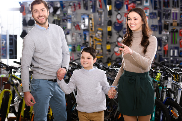 heureux jeune famille pointant du doigt et regardant loin dans magasin de vélo
 - Photo, image