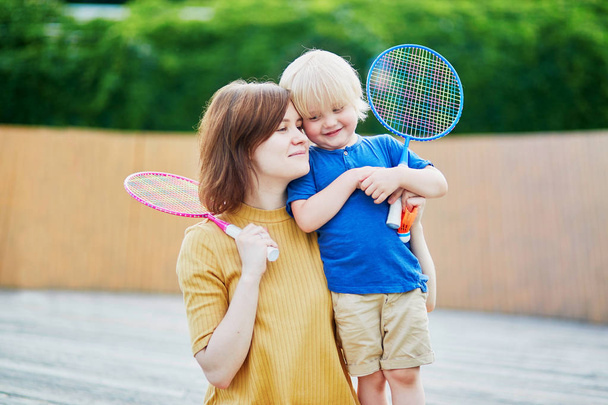 Adorable little boy playing badminton with his mother on the playground. Outdoor summer activities for kids. Family time together - Photo, Image