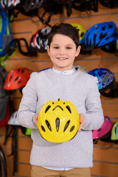 lindo niño sosteniendo casco y sonriendo a la cámara en la tienda de bicicletas
 - Foto, imagen