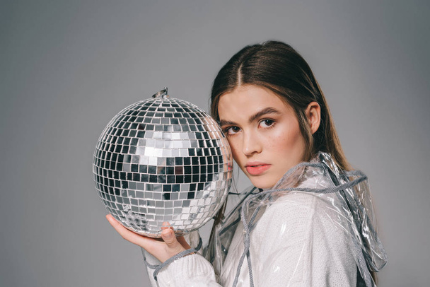 portrait of fashionable woman with disco ball in hands looking at camera isolated on grey - Zdjęcie, obraz