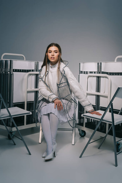 divatos nő fehér ruhát pózol a szürke háttér mögött összecsukható székek  - Fotó, kép