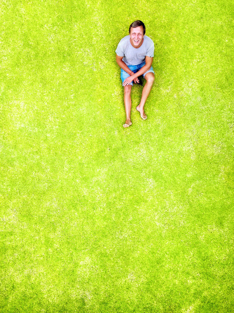 Um homem deita-se num relvado verde e sorri de felicidade. Vista superior e aérea com espaço de cópia. Mínimo estilo flat lay isolado no fundo de grama verde original
. - Foto, Imagem