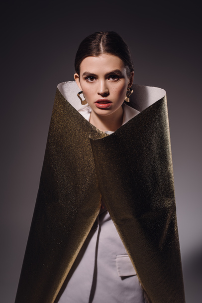 portrait of fashionable woman in golden wrapping paper posing on dark backdrop - Фото, изображение