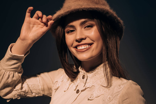 portrait of fashionable smiling woman in stylish hat looking at camera isolated on black - Photo, Image