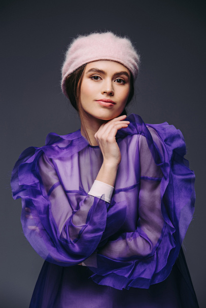 portrait of beautiful woman in fashionable purple dress and hat looking at camera on black background - Foto, Imagem
