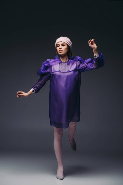 attractive woman in purple dress and hat posing on black background - 写真・画像