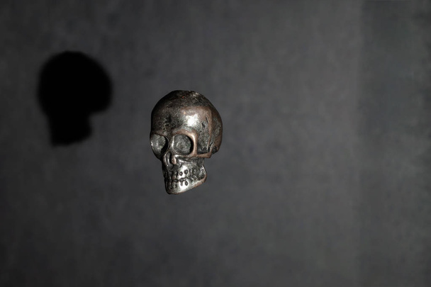 Crâne métallique lévitant dans l'air sur fond noir éclairé par la lumière et réfléchissant l'ombre sur fond
 - Photo, image