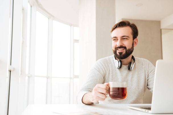 Attractive man with short brown hair and beard, drinking tea and - Foto, afbeelding