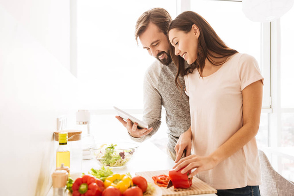 Portrait of a cheerful young couple cooking salad - Fotoğraf, Görsel