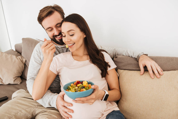 Cheerful young pregnant couple relaxing on a couch - Foto, Imagem