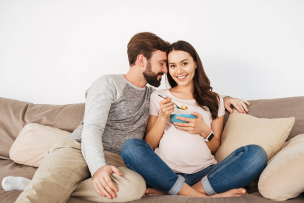 Lovely young pregnant couple relaxing on a couch together - Fotó, kép