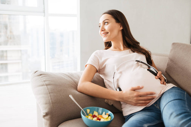 Happy pregnant young woman holding headphones - Fotó, kép