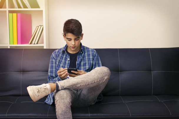 children, teenager or preteen with the mobile phone sitting on the couch - Photo, Image