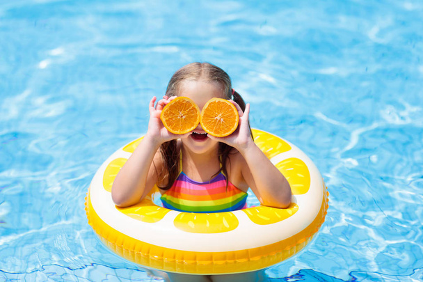 Child in swimming pool. Kid eating orange. - Fotoğraf, Görsel