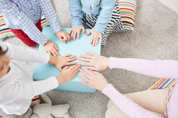 Jovem mulher e três crianças colocando as mãos na tampa da caixa grande enquanto joga no chão
 - Foto, Imagem