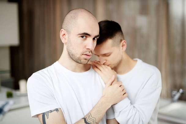 Young gay man looking at camera with his desperate partner head on his shoulder - Foto, Imagen