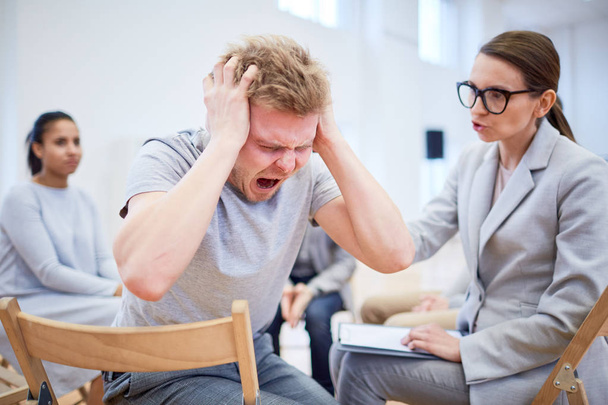Harmillinen tai stressaantunut nuori mies huutaa, kun psykologi yrittää tukea häntä istunnon aikana
 - Valokuva, kuva