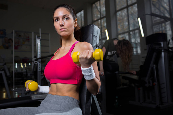 junge sportliche Frau mit Kurzhanteln, die im Sportverein oder Fitnessstudio trainiert - Foto, Bild