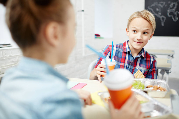 Cute schoolboy talking to one of classmates during lunch between lessons - Foto, Bild