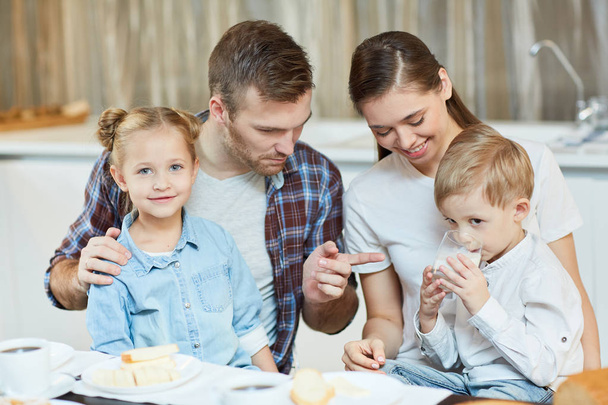 Junger Vater zeigt beim Familienfrühstück auf Milchglas seines kleinen Sohnes - Foto, Bild